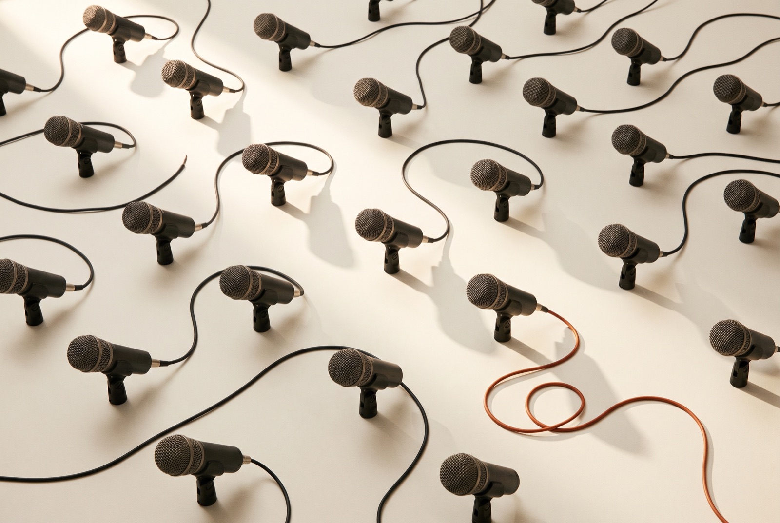 A grid of identical black studio microphones, one of them connected by a single burnt-orange cable