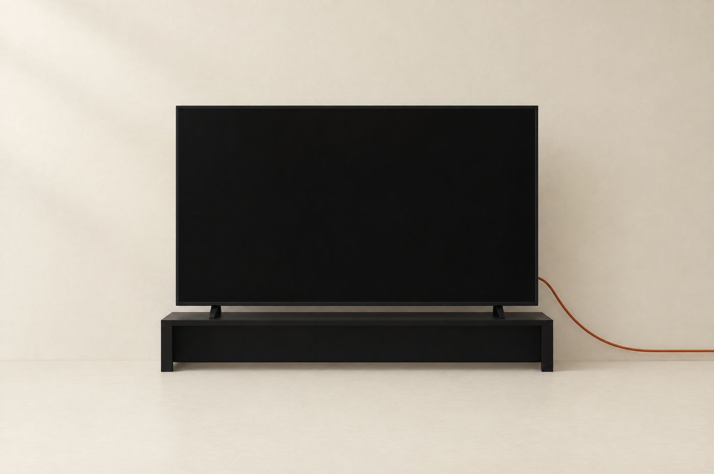 A switched-off black television on a low stand against a cream wall, a single burnt-orange audio cable running out of frame