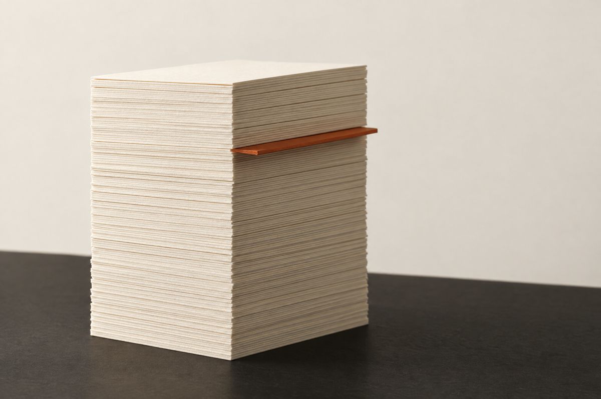 A tall stack of several hundred cream index cards on a black surface, a single burnt-orange card protruding a third of the way down